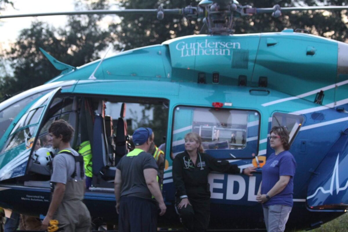 A group of people, including medical personnel, standing next to a teal and blue medivac helicopter with 