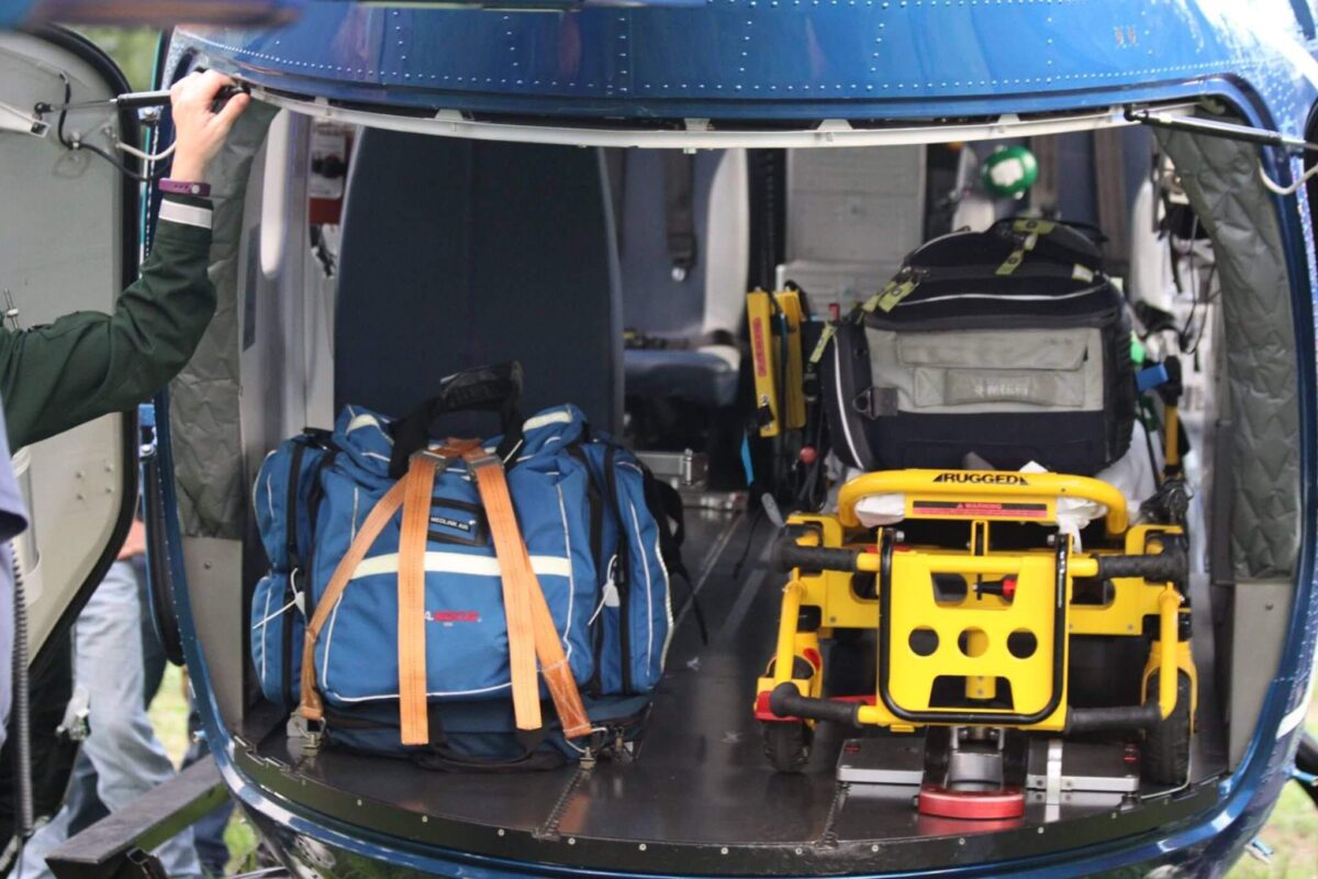 Inside view of a helicopter showing a blue duffel bag with brown straps on the left and a secured stretcher with medical equipment on the right. The interior is designed for medical transport, with equipment and supplies arranged for emergency use.