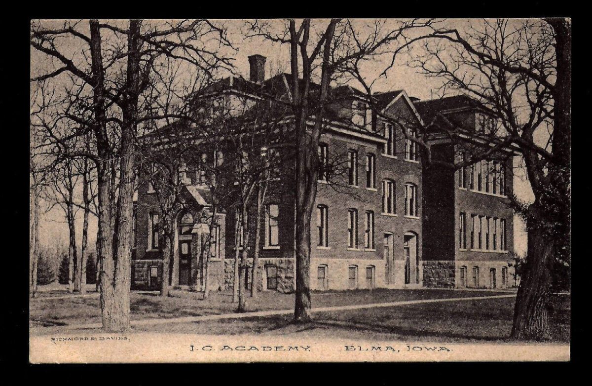 A sepia-toned vintage postcard image of a large, multi-story brick building labeled 