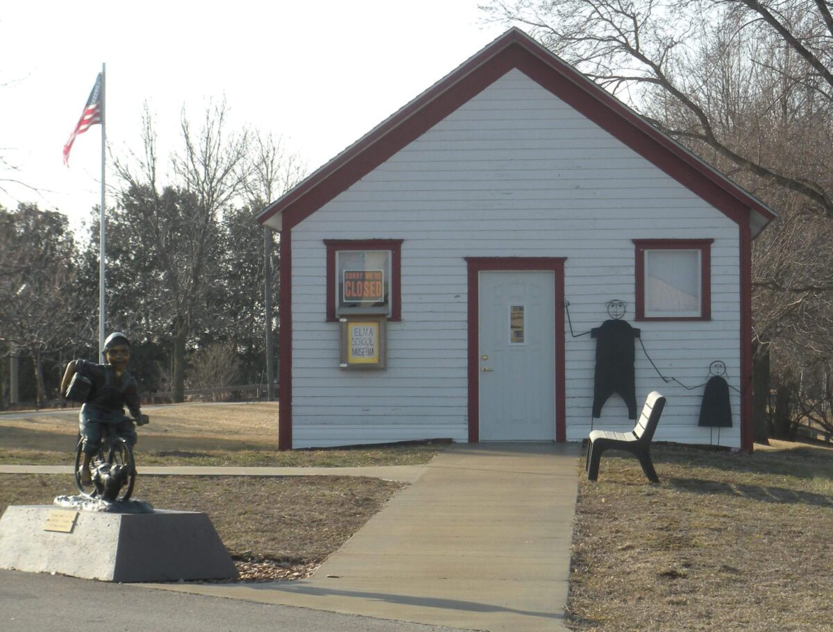 A small, white wooden house with red trim stands in the background, displaying a 