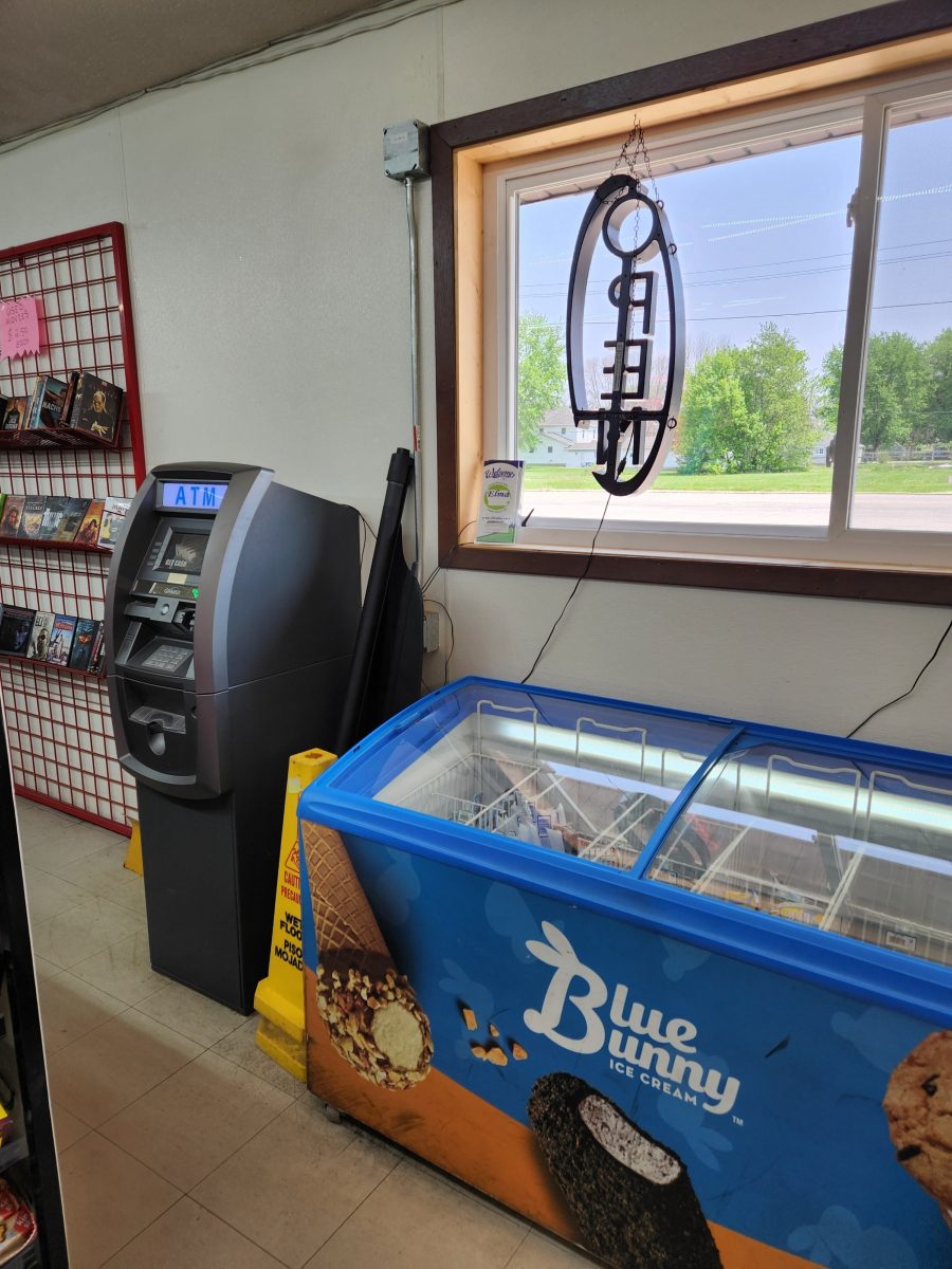 A convenience store corner featuring an ATM next to a Blue Bunny ice cream freezer. A 